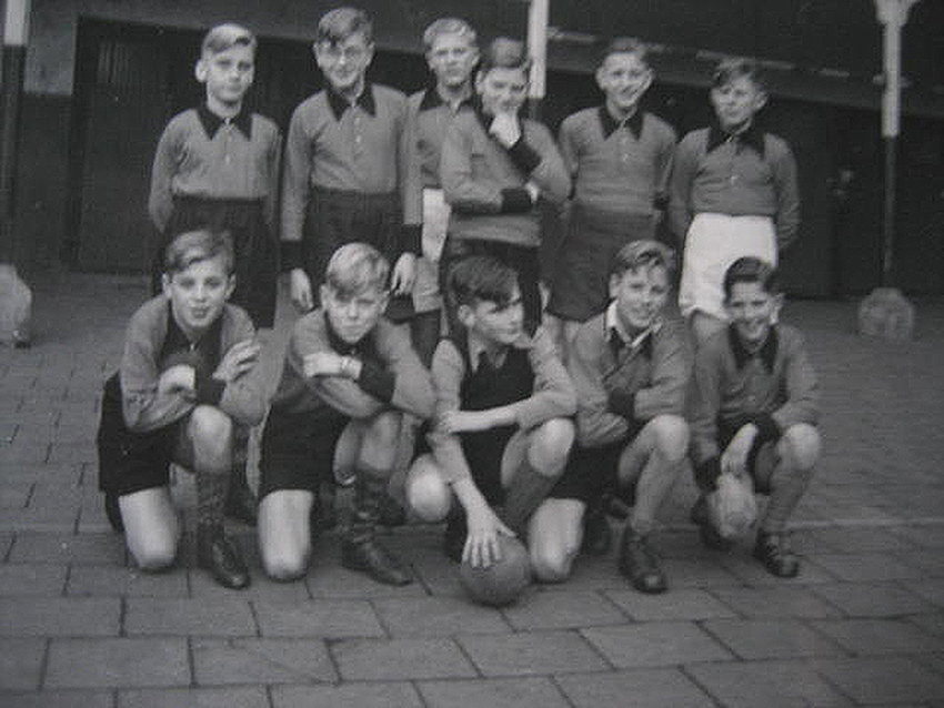 1. Voetbalploeg van onze klas, ca. 1955. Achter, derde van links is leerling Smits. Achter, tweede van rechts is leerling Brans. De foto is genomen voor het afdak achter op de speelplaats. Onder dat afdak waren ook de wc’s.