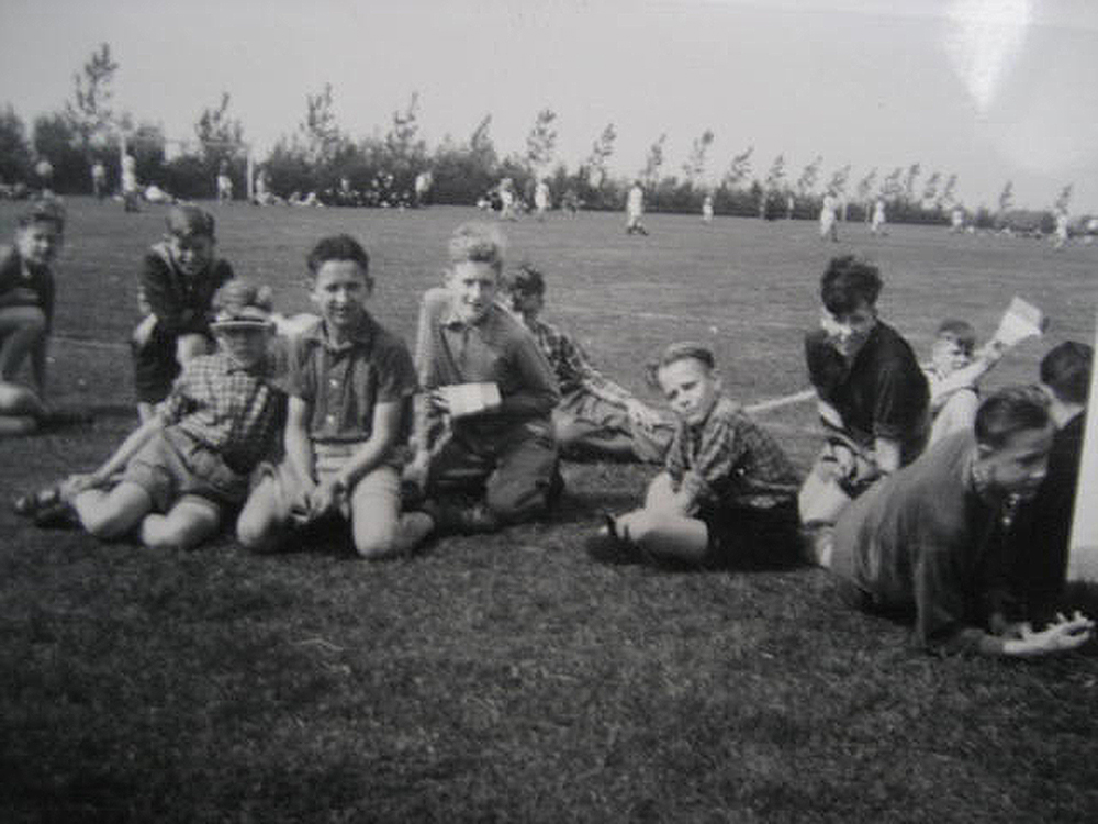 6. Henk van Meel en andere internen als toeschouwers van een voelbalwedstrijd van – waarschijnlijk – een schoolteam op de velden in Oss, 1955.