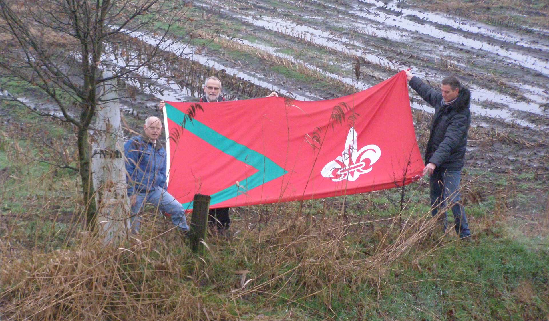 Initiatiefnemer Mike in ’t Groen (midden) samen met Jan Bastiaansen (links) en Toine Graumans (rechts) met de Rijsbergse vlag bij Grenspaal nr. 221 op de grens van Zundert-Rijsbergen-België (foto: Charles Luijten)