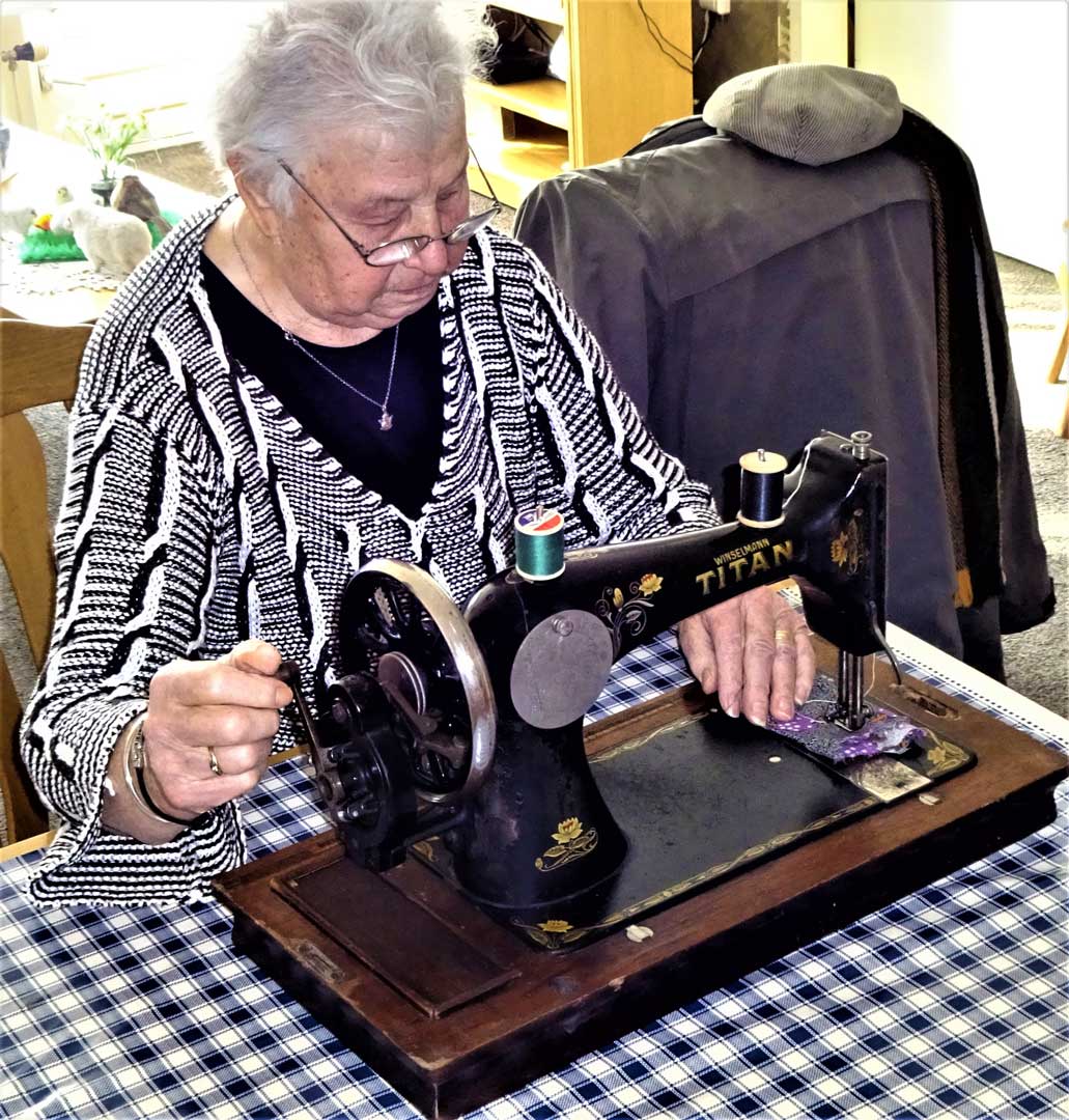 Diny, onlangs achter de Naaimachine. Haar dochter (60) vult aan: ’wat leuk, op deze, Oma’s naaimachine heb ik leren naaien.’  De machine is uit te breiden naar trapnaaimachine, op de voorzijde bevindt een maatverdeling in cm en Engelse duim.