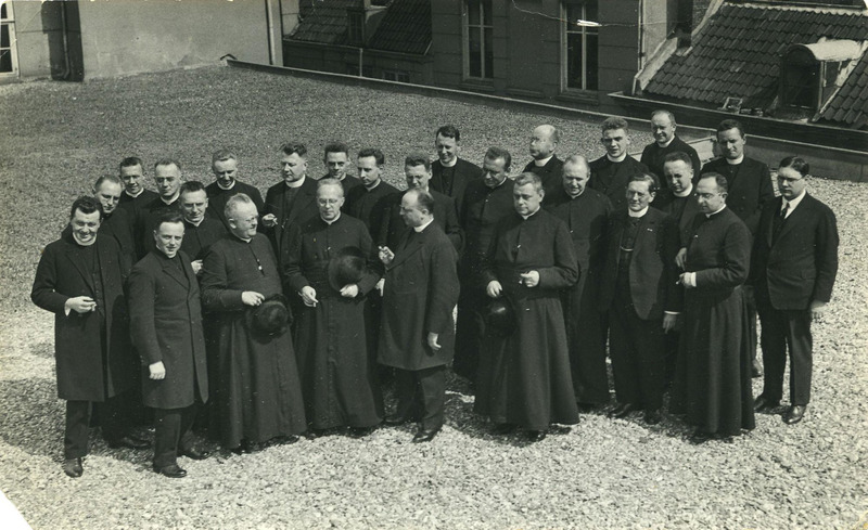 Rooms Katholieke geestelijken staan op het dak tijdens een bezoek aan De Maasbode, 1929. In het midden, met een sigaar in de hand, de met een lorgnet getooide mgr Jan Witlox, de hoofdredacteur van het roomsch-katholieke dagblad "De Maasbode" (bron: BHIC, fotonummer 1910-002100)